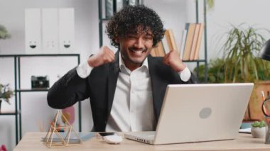 Indian businessman fingers crossed working on laptop at home office desk typing browsing say Wow yes found out great big lottery jackpot win, good job news, celebrating. Manager freelancer arab man