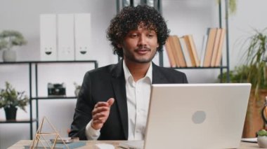 Indian businessman working on laptop computer at home office desk talk on online communication video call with employee, boss. Manager man freelancer support services looking at webcam of computer