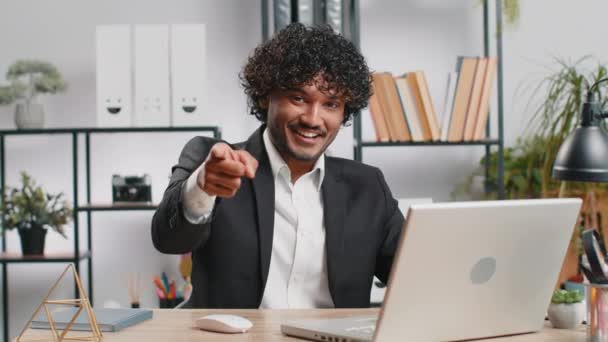 君を選んだ 若いインドのビジネスマンプログラマーソフトウェア開発者は カメラを指してオフィスのラップトップで作業し 幸せな表情で探し 選択をし 方向性を示しています アラブのフリーランスの男 — ストック動画