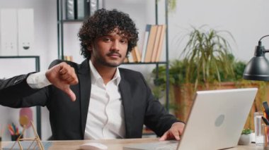 Hoşlanmamak. Merkez ofisteki dizüstü bilgisayarda çalışan üzgün Hintli işadamı hoşnutsuzluğunu, memnuniyetsizliğini ve kötü işini ifade eden işaret hareketini kabul etmiyor. Memnuniyetsizlik ciddi serbest çalışan adam