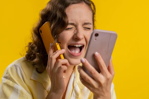 二つの携帯電話で会話の紛争の苦情の紛争の議論の問題を解決する議論を持って叫んで話す若い女性を強調した刺激的な神経 黄色のスタジオの背景に隔離された女の子 — ストック写真