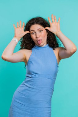 Komik, şakacı, genç bir kadın aptalca yüz ifadeleri takınıyor, suratını buruşturuyor, etrafta takılıyor, dil gösteriyor, aptalca bir ifade sergiliyor. Mavi stüdyo arka planında tek başına kalan bir kız. Yaşam tarzları. Dikey