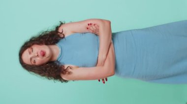 Neşeli, komik, genç bir kadın kameraya bakıp surat asıyor, şakalaşıyor, aptal suratıyla maymun taklidi yapıyor, alay ediyor, zorbalık yapıyor, taciz ediyor. Mavi stüdyo arka planında izole edilmiş bir kız. Yaşam tarzları. Dikey