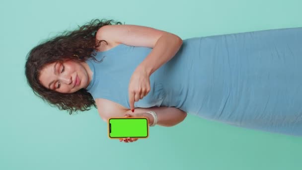 拥有绿色屏幕彩色键模拟智能手机的年轻开发人员女商人推荐了很好的应用程序促销产品 自由撰稿人女孩被隔离在蓝色的工作室背景 垂直方向 — 图库视频影像