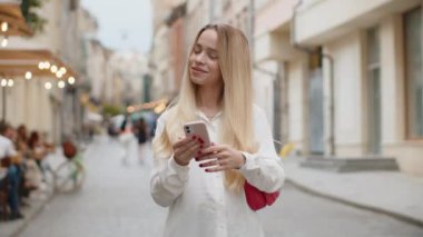 Gülümseyen genç bir kadın akıllı telefon kullanıyor mesajlar yazıyor internette geziniyor, işi bitiriyor, dışarıdaki kameralara bakıyor. Şehir caddesinde yürüyen genç bir turist kız. Kasaba yaşam tarzları