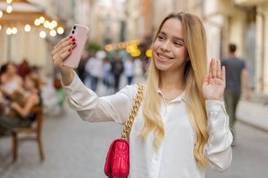 Sarışın genç kadın blogcu akıllı telefondan selfie çekiyor, abonelerle çevrimiçi video görüşmesi yapıyor, sosyal medya vlog 'u için hikayeler kaydediyor. Şehir caddesinde yürüyen genç kız