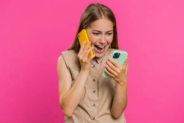 イライラした神経症は 2台の携帯電話で話す若い女性が会話の紛争の争いの論争で問題を議論することを強調しました ピンクのスタジオの背景に孤立した少女 — ストック写真