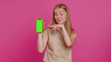 Genç müteahhit iş kadını elinde yeşil ekran krom tuşlu akıllı telefon ile iyi bir uygulama tanıtım satış teklifi sunuyor. Serbest çalışan sarışın yetişkin kız pembe stüdyo arka planında izole edilmiş.