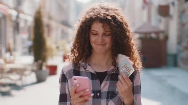 快乐富有的年轻女性数钱 使用智能手机计算器应用程序 计划在网上订购礼物和食品 预订酒店房间 漂亮的女孩游客在城市街道上 — 图库视频影像