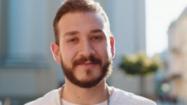 Mutlu sakallı genç bir adamın portresi. Dostça gülümseyen, kameraya bakan mutlu yüz ifadesi. Hayal kuran, dinlenen, rahatlayan. Şehir Güneşi Sokağı arka planındaki adam