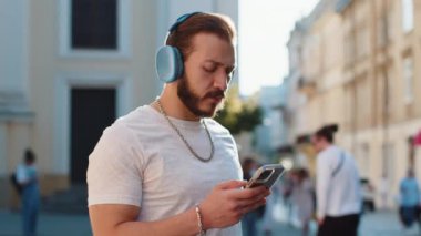 Kablosuz kulaklıklı, neşeli sakallı mutlu genç adam dışarıda dans eden enerjik disko rock 'n roll müziğini dinliyor. Şehir güneşinde yürüyen adam kalabalık bir şehir caddesinde yürüyor.
