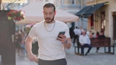 Para sayan mutlu genç bir adam, akıllı telefon hesap makinesi uygulaması, internetten hediye ve yemek siparişi verme planı, otel odası rezervasyonu. Şehir caddesinde sakallı bir turist. Şehir dışında.