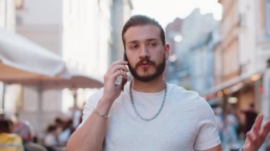 Erkek turistin uzaktan konuşma portresi akıllı telefondan arkadaşlarıyla iletişim kuruyor, şehir caddesinde beklenmedik bir şekilde iyi haber dedikodusu yapıyor. Şehir yaşam tarzları açık havada