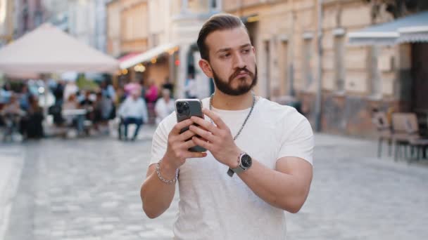 Jovem Barbudo Sorrindo Usando Smartphone Digitando Mensagens Texto Navegando Internet — Vídeo de Stock
