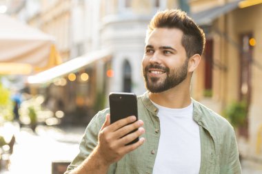Mutlu, gülümseyen sakallı genç adam internet sosyal medya uygulamalarını karıştırarak dışarıda sohbet ederek akıllı telefon yazıları yazıyor. Şehir caddesinde yürüyen bir turist. Kasaba yaşam tarzları