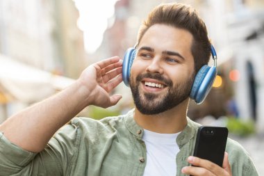 Kablosuz kulaklıklar takmış, açık havada dans eden enerjik disko rock n roll müziği dinleyen mutlu, gevşemiş Kafkas genci. Şehir Güneşi Sokağı arka planında duran adam.