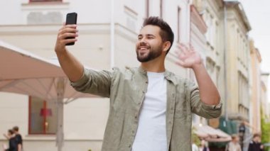 Sakallı genç blog yazarı akıllı telefondan selfie çekiyor, abonelerle ya da aile dostlarıyla çevrimiçi video görüşmesi yapıyor, sosyal medya vlog 'u için hikayeler kaydediyor. Şehir caddesinde yürüyen adam