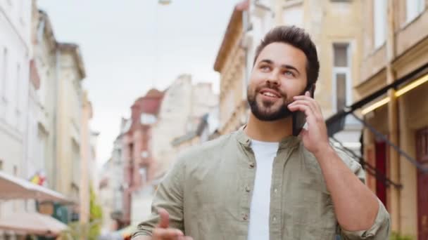 快乐的年轻人游客通过智能手机与人进行远程交流 满嘴胡子的家伙在电话里说着意想不到的好消息 流言蜚语在城市街道上流传 户外城镇生活方式 — 图库视频影像