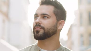 Mutlu genç adamın yakın plan portresi gülümseyen arkadaş canlısı, mutlu gözler kameraya bakıp dinlenen rahatlama hayalleri kuran açık havada iyi haberler veriyor. Güneşli şehir sokağındaki sakallı adam.