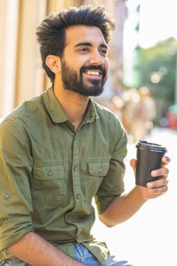 Mutlu Hintli adam sabah kahvesinin tadını çıkarıyor. Sıcak bir içecek, şehir hayatı tarzında. Dinleniyorum, ara veriyorum. Dışarıdaki şehir merkezi caddesinde oturan gülümseyen Arap müslüman adam. Dikey