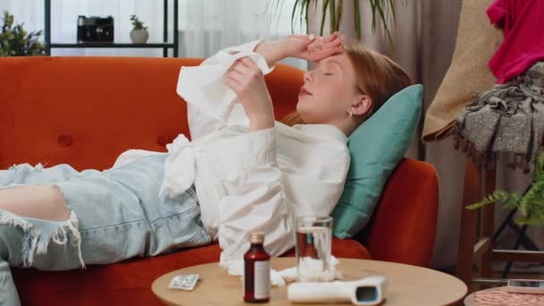 ティーンエイジャー病の赤い髪の少女は 自宅のリビングルームのソファーに横たわって風邪やアレルギーに苦しんでいます 病気の子供はナプキンにスニッツワイプを吹きます コロナウイルス検疫 パンデミック インフルエンザ ライフスタイル — ストック動画