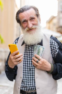 Zengin, yaşlı ve zengin bir adam elinde bir dolar nakit para tutuyor, akıllı telefon hesap makinesi uygulaması kullanıyor, hediye siparişi vermeyi planlıyor, internetten yemek siparişi veriyor, otel odası ayırtıyor. Yaşlı büyükbaba turist şehir caddesinde