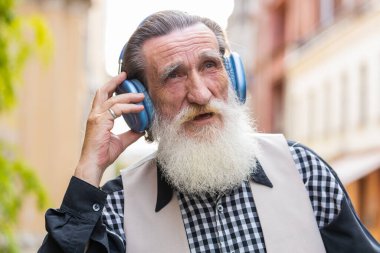 Neşeli, gevşemiş, sakallı, kablosuz kulaklıklı yaşlı adam dışarıda dans eden enerjik disko rock 'n roll müziğini dinliyor. Yaşlı büyükbaba şehir caddesinde yürüyor