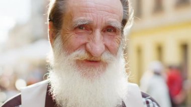 Mutlu sakallı yaşlı bir adamın portresi dostça gülümsüyor, kameraya bakan mutlu yüz ifadesi hayal kuruyor, dinleniyor, rahatlıyor dışarıda iyi haberler veriyor. Şehir caddesinde olgun büyükbaba