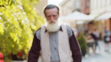 Öfkeli, sakallı, yaşlı adam, mutsuz, tatminsiz birini üzdü. Nefret dolu suratlı agresif yaşlı büyükbaba kameraya bakıyor. Hayal kırıklığına uğramış, sinirli, sinirli, sinirli, şehir caddesinde duruyor.