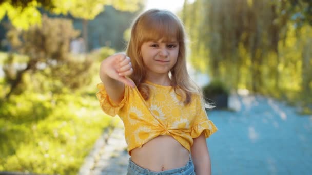 気に入らない 子供が親指を下に示し 不満の不満の不満の悪い仕事の間違いを表現する 街の日没公園の通り 屋外に立っている不満の金髪の少女 — ストック動画