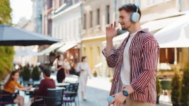 Kablosuz kulaklıklı, neşeli sakallı mutlu adam dışarıda akıllı telefondan dans ederek en sevilen enerjik disko müziğini dinliyor. Şehir merkezinin önünden geçen turist.