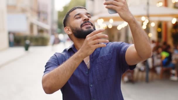 有胡子的印度男子博主在智能手机上自拍 与订户或家人朋友在网上进行视频通话 在室外为社交媒体Vlog记录故事 走在城市街道上的家伙 — 图库视频影像