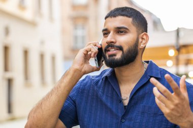 Hintli Arap erkek turist uzaktan iletişim kuruyor. Akıllı telefondan arkadaşlarıyla konuşuyor. Şehir caddesinde beklenmedik iyi haber dedikoduları yapıyor. Şehir yaşam tarzları açık havada