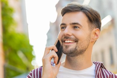 Sakallı, genç, yetişkin bir turistin portre yüzü. Uzaktan iletişim kuruyor. Akıllı telefondan arkadaşlarıyla konuşuyor.