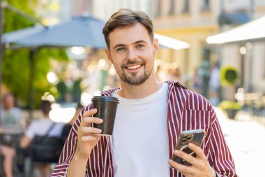 Mutlu sakallı adam sabah kahvesinin tadını çıkarıyor sıcak içeceği içiyor ve dışarıda kameraya bakıp gülümsüyor. Dinlenmeye çalışıyorum. Şehirdeki Sunshine Caddesi 'nde yürüyen ve kahve içen bir adam. Kasaba yaşam tarzları
