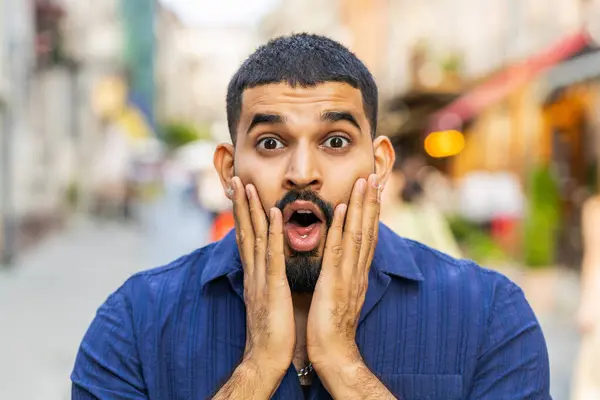 Oh my God, Wow. Bearded indian man looking surprised at camera with big open eyes, shocked by sudden victory, game winning, lottery goal achievement, good news outdoors. Guy in city sunshine street