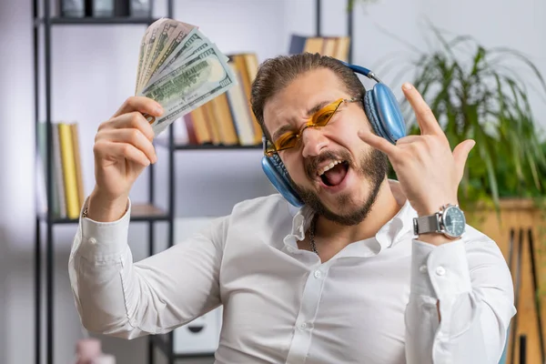 Lebanese businessman holding fan of cash money dollar banknotes celebrate, dance, success career, lottery jackpot game winner, big income, wealth at home office workplace desk. Remote distant working