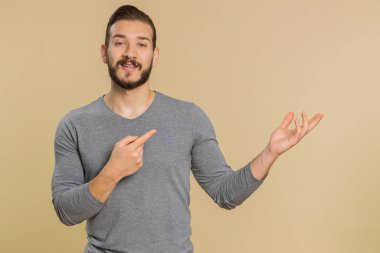 Lübnanlı genç adam onaylıyor ve boş bir yeri işaret ediyor. Ticari metinler için reklam alanı, ürün tanıtım logosu için kopyalama alanı. Orta Doğulu adam bej renkli stüdyo arka planında izole edilmiş.