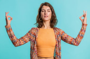 Sakin ol, rahatla, iç denge. Genç kadın derin nefes alıyor Mudra jesti, gözleri kapalı, konsantre düşüncelerle meditasyon yapıyor, huzurlu bir zihin. Mavi arka planda izole edilmiş çekici bir kız.