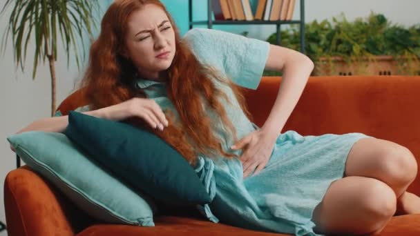 期間のけいれんに苦しむ病気の赤毛の女性は 痛みを伴う胃の痛みを自宅のソファの上に横たわる 女の子は腹を持っています 腹部や月経痛を感じます 腹部の痛み 消化不良 — ストック動画