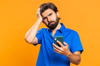 Adam cep telefonu akıllı telefon daktilosu kullanıyor. Ani piyango sonuçlarını kaybediyor. Kötü talih, kayıp. Orta Doğulu tişörtlü adam turuncu stüdyo arka planında tek başına kapalı bir yerde.