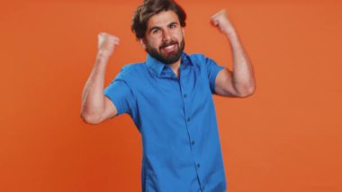 Mutlu, mutlu, gülümseyen adam başarıyı kutluyor, doğum gününü kazanıyor, piyango vurgunu hedefini tutturuyor, oyun oynuyor, iyi haberler, zafer. Turuncu stüdyo arka planında genç bir ortadoğulu.