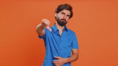 Hoşlanmamak. Mutsuz genç bir adam, hoşnutsuzluğunu, memnuniyetsizliğini, hoşnutsuzluğunu, hoşnutsuzluğunu ifade ederek işaret ediyor. Yakışıklı bir ortadoğulu. Turuncu stüdyo arka planında kapalı alan