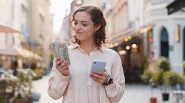 Para sayan mutlu genç bir kadın, akıllı telefon hesap makinesi uygulaması, planlanmış tatil hediyeleri için gelir memnuniyeti. Şehir merkezinde güneşli bir sokakta yürüyen güzel bir kız. Şehir yaşam tarzları açık havada