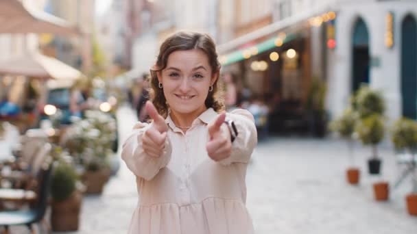 快乐的年轻漂亮的女人赞许地看着展示大拇指的相机 就好像是积极的信号 积极的反馈 可爱的女孩走在城市街道上 户外城镇生活方式 — 图库视频影像