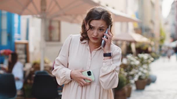 激しい緊張の中 2台の携帯電話で会話をしている若い女性が大声で叫んでいるのを強調し 苦情紛争の議論は屋外で問題を解決する 都会の街を歩く女の子 — ストック動画