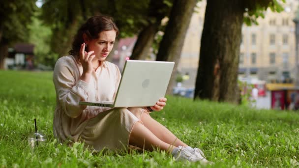 年轻女性的肖像用笔记本电脑打字上网工作 失去了意想不到的突然中彩票结果 坏消息 财富损失 女孩坐在城市日落城市公园的草地上 — 图库视频影像