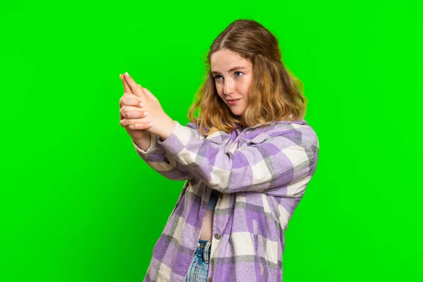 Young woman pointing around with finger gun gesture, looking confident, making choice, shooting killing with hand pistol right on target. Girl isolated on green chroma key background. Advertisement