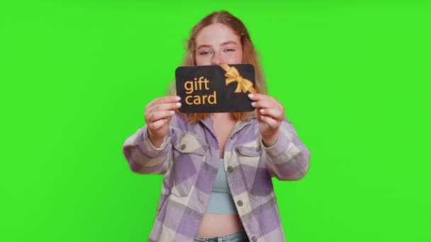 店の休日の販売のためのギフト割引証明書のバウチャーのクーポンを指すことを示す幸せな白人女性 ショッピングクリスマスのサプライズカードを緑色のクロマキーの背景に分離した赤毛の少女 — ストック動画