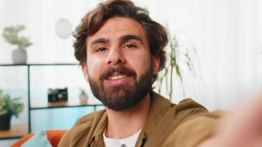 Ortadoğu blogcusu akıllı telefondan selfie çekiyor abonelerle internet üzerinden video görüşmesi yapıyor, sosyal medya için hikayeler kaydediyor. Ev odasındaki sakallı Arap adam.